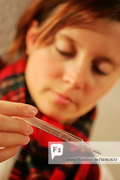Gesundheit  Kälte  Krankheit. Junge Frau misst ihre Blutwärme mit einem Fieberthermometer