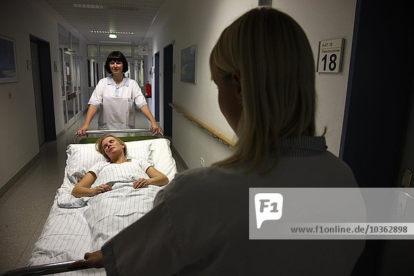 Patientin wird von Krankenschwestern in ihrem Bett über einen Krankenhausboden bewegt