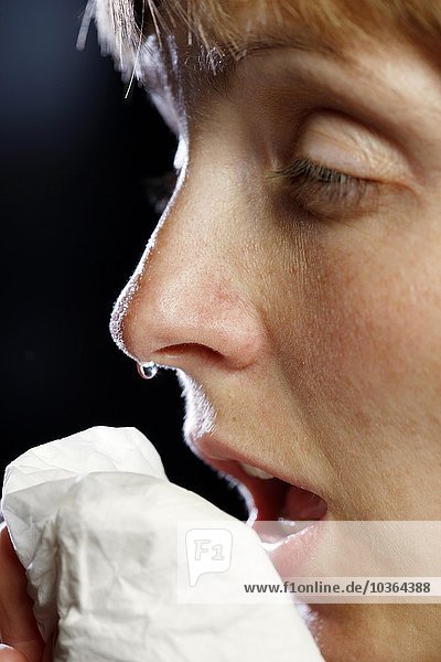 Junge erwachsene Frau hat Schnupfen  muss niesen  putzt sich die Nase mit einem Taschentuch. Die Nase tropft