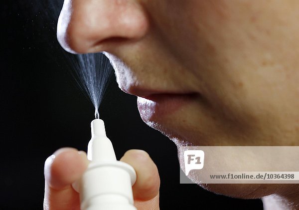 Junge erwachsene Frau sprüht sich ein Spray in die Nase  gegen Schnupfen  verstopfte Nase bei Heuschnupfen zum Beispiel