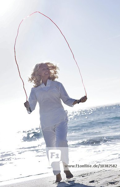 Ältere Frau hüpft am Strand