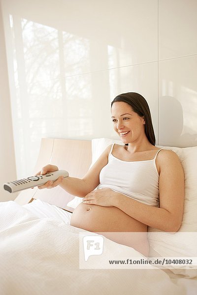 Schwangere Frau sieht im Bett fern