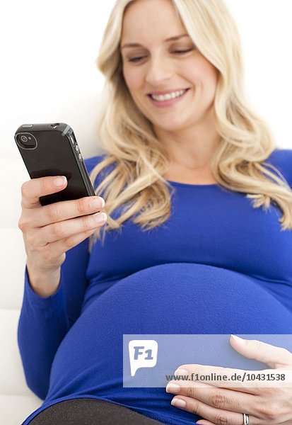 MODELL FREIGEGEBEN. Schwangere Frau bei der Benutzung eines Mobiltelefons. Sie ist im 8. Monat schwanger.