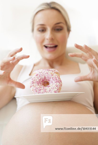 MODELL FREIGEGEBEN. Schwangere Frau mit einem Teller Krapfen. Sie ist im 8. Monat schwanger.