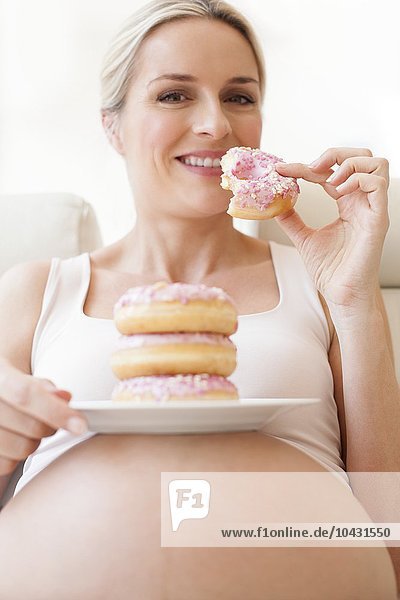 MODELL FREIGEGEBEN. Schwangere Frau isst einen Teller mit Donuts. Sie ist im 8. Monat schwanger.