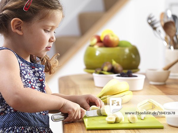 MODEL RELEASED. Young girl cutting a banana. Three year old girl preparing herself a snack.