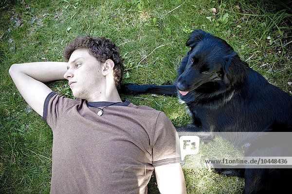 boy lying on the grass with a dog on the side