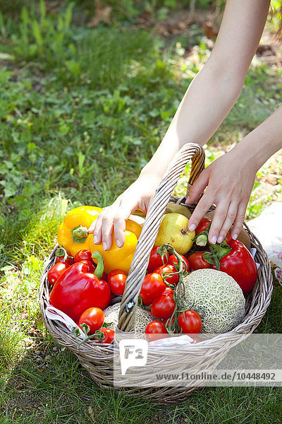 Hände einer Frau auf einem Korb mit Gemüse in einem Garten