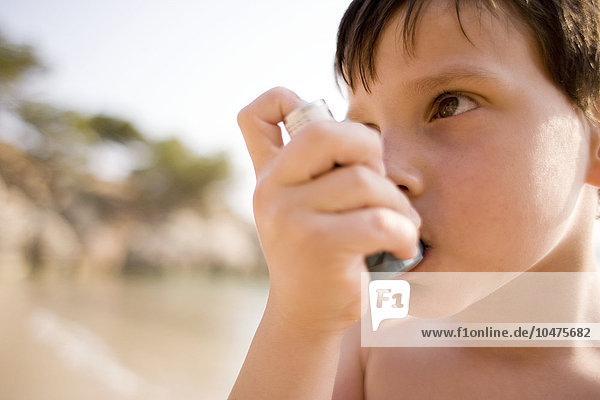 MODELL FREIGEGEBEN. Asthmatischer Junge benutzt seinen Inhalator am Strand Asthmatischer Junge