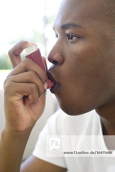 MODELL FREIGEGEBEN. Verwendung eines Asthma-Inhalators. Ein Mann benutzt einen Inhalator zur Behandlung eines Asthmaanfalls. Asthma ist eine Erkrankung  bei der sich die kleinen Atemwege (Bronchiolen) in der Lunge verengen und das Atmen erschweren. Dies führt zu Keuchen  Husten und Atemnot. Der Inhalator enthält bronchienerweiternde Medikamente  die die Atemwege erweitern. Asthma-Inhalator