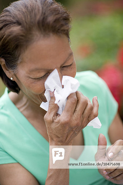 MODELL FREIGEGEBEN. Niesende Frau. Bild 2 von 2: Eine Frau niest in ein Taschentuch. Sie hat eine Erkältung  eine Virusinfektion  die eine Entzündung der Nasen- und Rachenschleimhäute verursacht hat. Niesen ist eine reflexartige Reaktion des Körpers  um Fremdkörper oder überschüssigen Schleim aus den Atemwegen zu entfernen. Eine Sequenz dieser niesenden Frau finden Sie in den Bildern M130/844-845. Niesende Frau