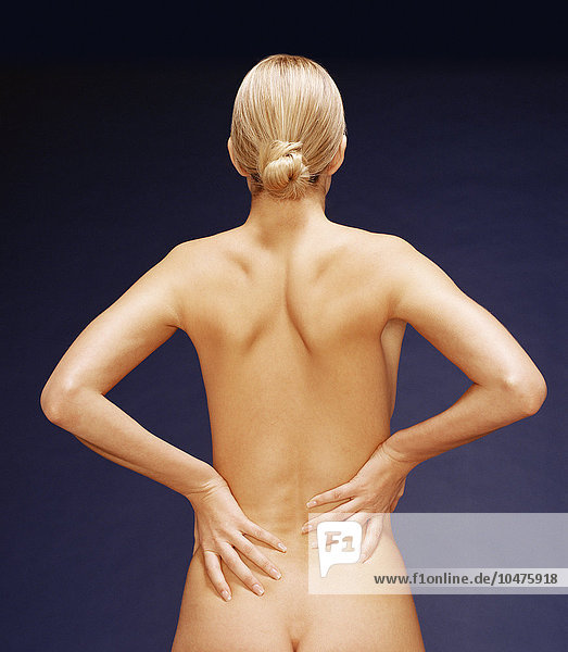 MODELL FREIGEGEBEN. Schmerzen im unteren Rücken. Frau reibt sich den schmerzenden unteren Rücken. Bei den Schmerzen im unteren Rücken könnte es sich um einen Hexenschuss handeln  bei dem die Weichteile um die Knochen der Wirbelsäule überlastet sind. Dies kann durch unsachgemäßes Heben schwerer Lasten verursacht werden. Die Behandlung umfasst Ruhe und schmerzstillende Medikamente. Schmerzen im unteren Rücken