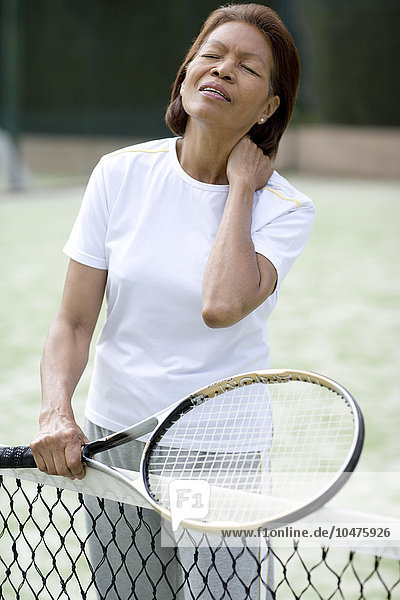 MODEL RELEASED. Painful neck injury. Woman holding her shoulder in pain during a game of tennis. She may have pulled a neck or shoulder muscle while serving or hitting the ball. Gentle stretching exercises before and and after sporting activities can help to avoid such injuries. Painful neck injury