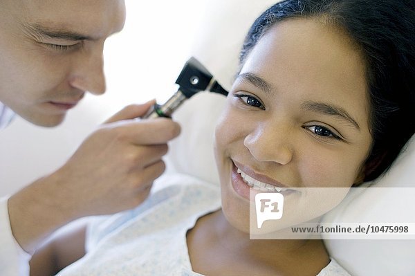 MODEL RELEASED. Ear examination. Doctor on a ward using an otoscope to examine a teenage girl's ear. Ear examination
