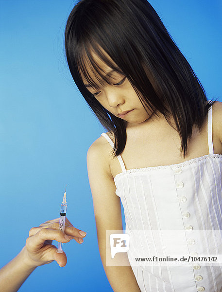 MODELL FREIGEGEBEN. Injektion in der Kindheit. 6-jähriges Mädchen schaut ängstlich auf eine Spritze Injektion in der Kindheit
