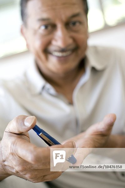 MODEL RELEASED. Blood glucose test. Man using a pen-like lancing device to prick his finger for a blood glucose test. Diabetics have to perform this test regularly. Diabetes is a metabolic disorder in which unused sugars accumulate in the blood and urine. Monitoring of blood glucose levels allows diabetics to control the disease through diet  medication and in some cases insulin injections. The pen is designed to make drawing blood less painful. Blood glucose test