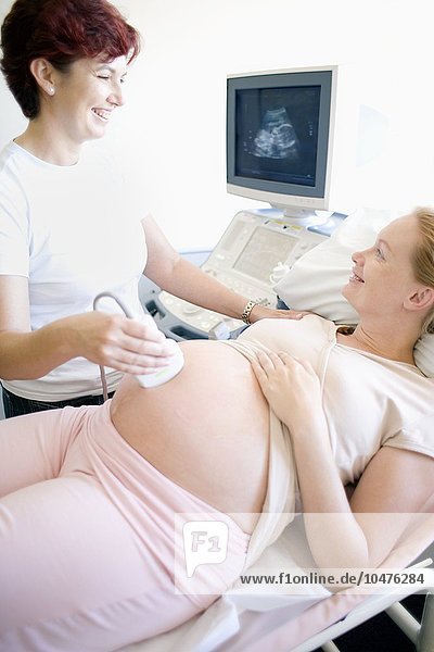 MODEL RELEASED. Obstetric ultrasound. Obstetrician using an ultrasound transducer to scan the abdomen of a pregnant woman. The transducer (held against the abdomen) emits high frequency sound waves that are echoed back and used to create an image of the foetus inside the mother's womb  which is displayed on a monitor. This is a safe non-invasive method of assessing the health ofthe developing foetus. Obstetric ultrasound