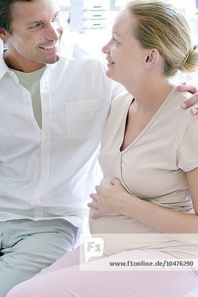 MODEL RELEASED. Expectant parents. Man sitting with his arm round his pregnant partner. Expectant parents