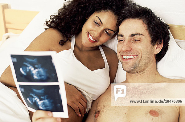 MODELL FREIGEGEBEN. Werdende Eltern sehen sich Ultraschallbilder ihres ungeborenen Kindes an. Mit Hilfe von Ultraschall können Bilder eines Fötus erstellt werden. Dabei werden Hochfrequenztöne durch den Unterleib geleitet und die Echos aufgezeichnet  um ein Bild des Fötus zu erstellen. Diese Technik ist nützlich  um die Gesundheit und das Wachstum des Fötus zu überwachen  und kann zur Geschlechtsbestimmung verwendet werden. werdende Eltern