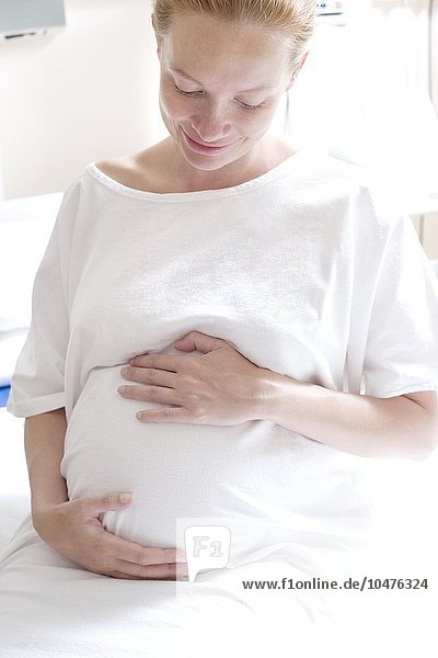 MODELL FREIGEGEBEN. Schwangere Frau auf einer Entbindungsstation  die ihren geschwollenen Bauch festhält Schwangere Frau