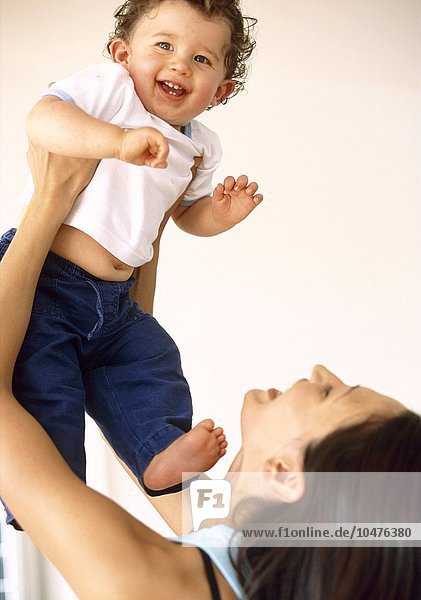 MODELL FREIGEGEBEN. Kleiner Junge und Mutter. 9 Monate altes Baby lächelt  als seine Mutter ihn über ihren Kopf hebt Baby und Mutter