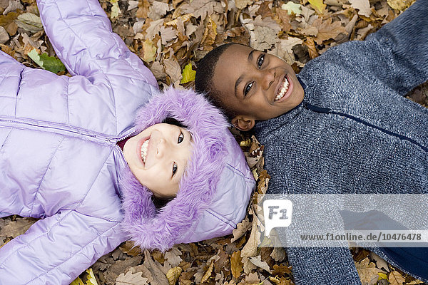 MODELL FREIGEGEBEN. Lächelndes Mädchen und Junge auf Herbstblättern liegend Lächelnde Kinder auf Herbstblättern liegend