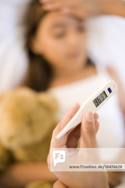 MODELL FREIGEGEBEN. Krankes Kind. Die Mutter liest ein elektronisches Thermometer ab  während sie die Temperatur ihrer Tochter mit der Hand kontrolliert Krankes Kind
