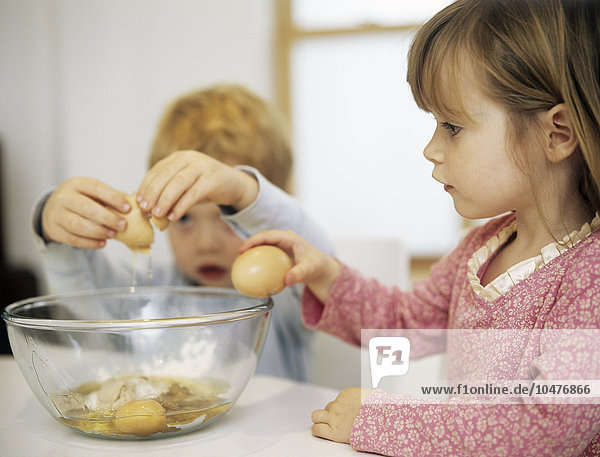 MODELL FREIGEGEBEN. Kuchen backen. Zwei dreijährige Kinder schlagen Eier an der Seite einer Rührschüssel auf und fügen sie einer Kuchenmischung hinzu Kuchen backen