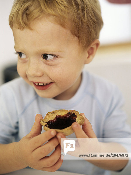 MODELL FREIGEGEBEN. Junge isst ein Marmeladentörtchen. Verarbeitete Versionen von süßen Lebensmitteln wie Marmeladentörtchen enthalten große Mengen an Zucker und Fett  und ein übermäßiger Verzehr kann bei Kindern zu Fettleibigkeit führen. Diese Lebensmittel können auch Zusatzstoffe  Farbstoffe und Konservierungsmittel enthalten  die andere Probleme wie hyperaktives Verhalten verursachen können. Eine Möglichkeit  dieses Risiko zu verringern  besteht darin  Kuchen  Kekse und andere Leckereien zu Hause zu backen und so die Menge an Zucker und künstlichen Zusatzstoffen  Konservierungsmitteln und Aromen zu kontrollieren. Dies kann auch eine wirksame Möglichkeit sein  Kindern mit bestimmten Lebensmittelallergien oder -unverträglichkeiten Leckereien anzubieten. Junge isst ein Marmeladentörtchen