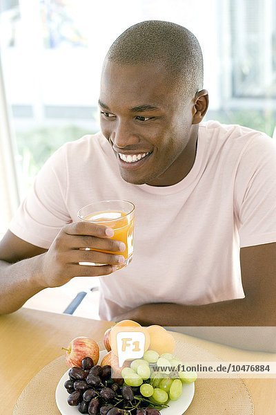 MODELL FREIGEGEBEN. Mann trinkt Orangensaft an einem Esstisch Mann trinkt Orangensaft