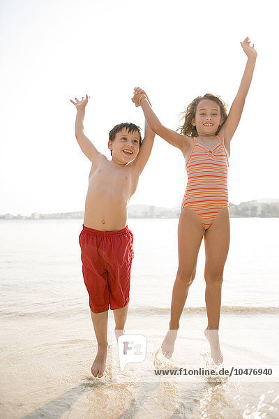 MODELL FREIGEGEBEN. Glückliche Kinder  die an einem Strand über die Wellen springen Glückliche Kinder