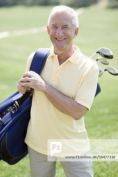 MODEL RELEASED. Golf player. Man carrying a bag of golf clubs on a golf course. Golf player