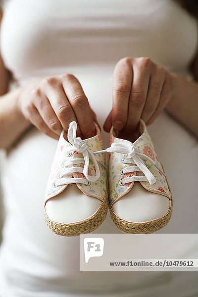 Schwangere Frau hält Babyschuhe
