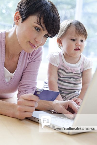 MODELL FREIGEGEBEN. Online-Einkauf. Mutter kauft online ein  während ihre 15 Monate alte Tochter zuschaut Online-Shopping
