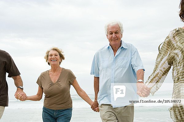 Vier ältere Erwachsene halten sich am Strand an den Händen.