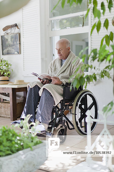Älterer Mann liest im Rollstuhl