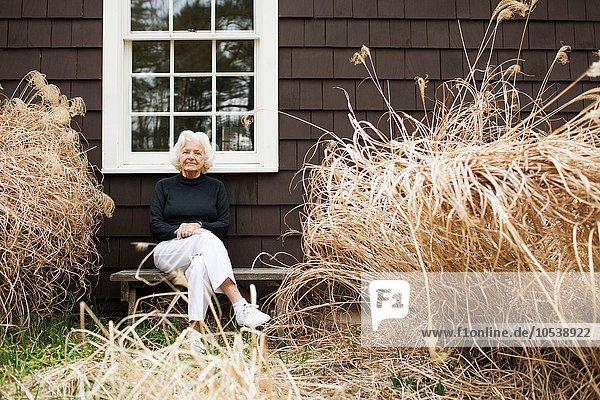 Porträt einer älteren Frau  die auf einer Bank vor dem Haus sitzt.