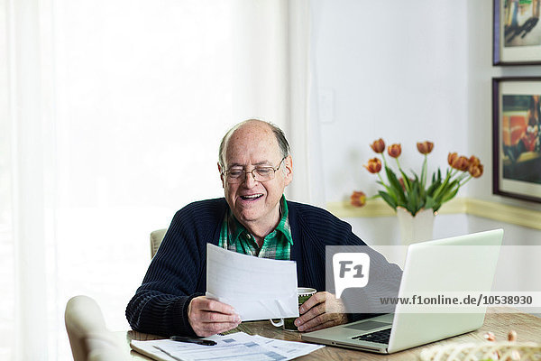 Älterer Mann  der sich Dokumente auf dem Schreibtisch zu Hause ansieht.