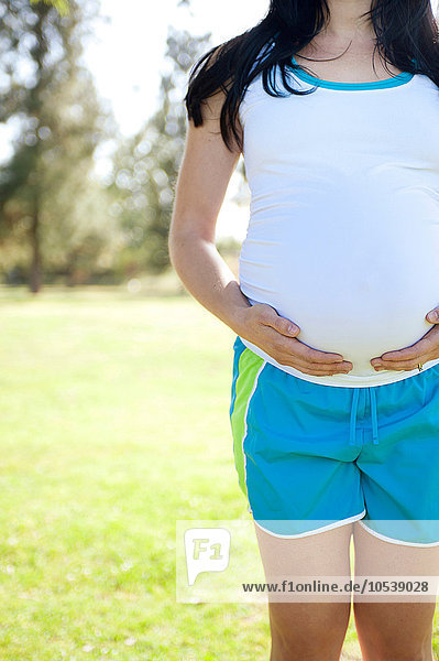 Schwangere junge Frau  die den Bauch berührt  Vorderansicht