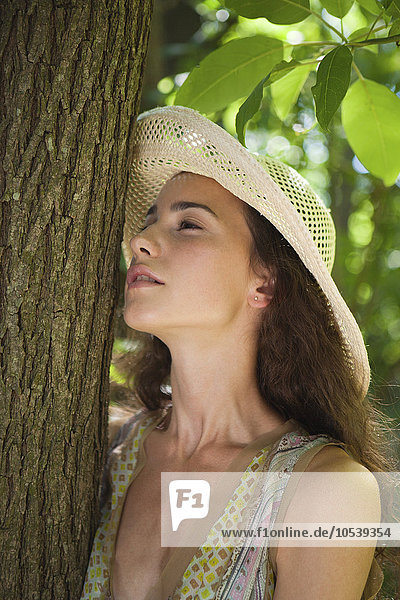 Junge Frau mit Sonnenhut an Baumstamm gelehnt  Portrait