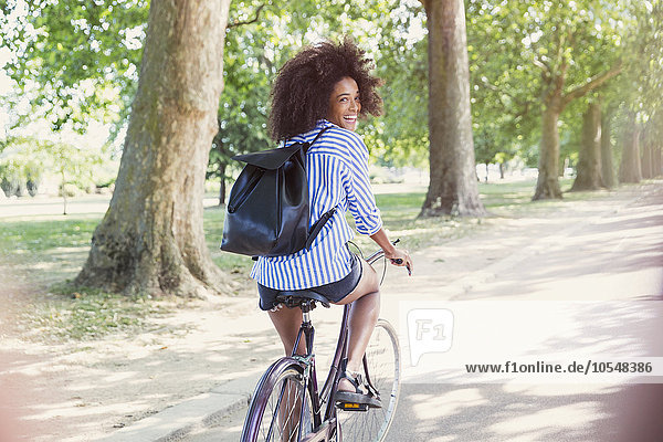 Portrait smiling woman with afro riding bicycle in park