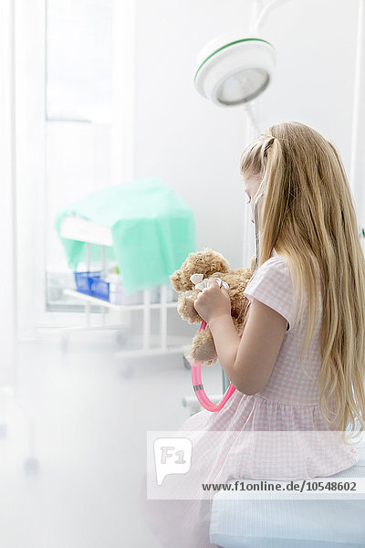 Girl using stethoscope on teddy bear in examination room