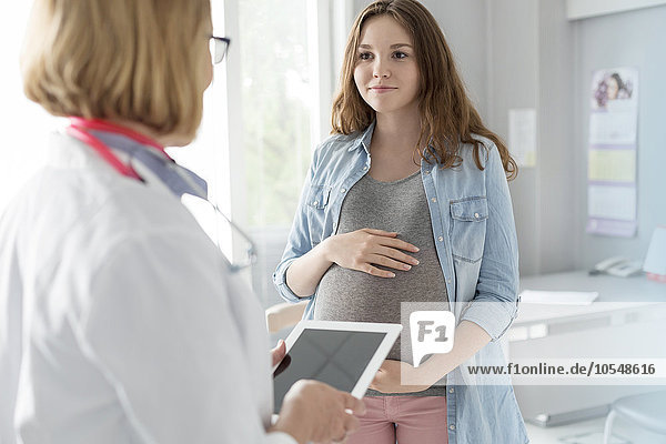 Arzt mit digitaler Tablette im Gespräch mit schwangeren Teenager-Patienten im Untersuchungsraum