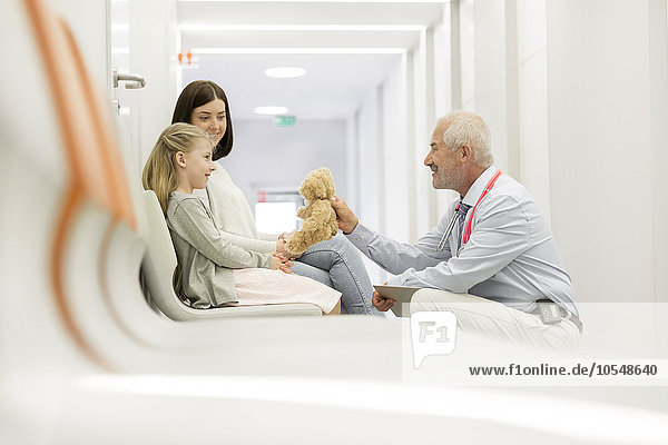 Doctor with teddy bear talking to girl patient in clinic corridor