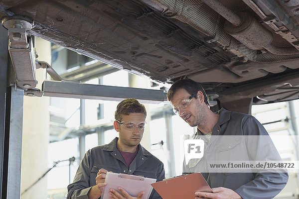 Mechaniker mit Klemmbrettern sprechen unter dem Auto in der Autowerkstatt