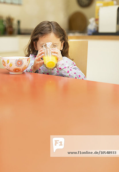 Mädchen trinkt Orangensaft am Frühstückstisch