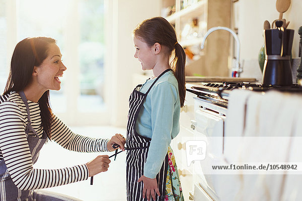 Mother tying apron on daughter in kitchen