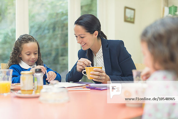 Arbeitende Mutter und Tochter bei den Hausaufgaben am Frühstückstisch