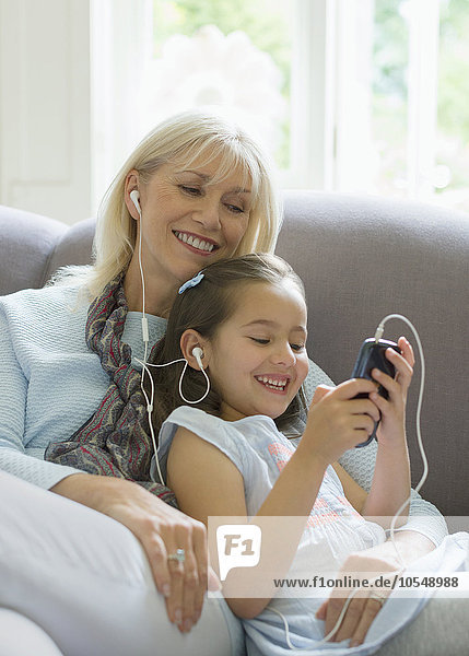 Großmutter und Enkelin teilen sich Kopfhörer und hören Musik auf dem Sofa.