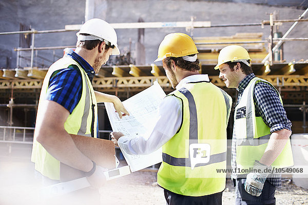 Bauarbeiter und Ingenieure bei der Begutachtung von Bauplänen auf der Baustelle